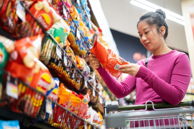A woman looking at a packet of crisps in the supermarket