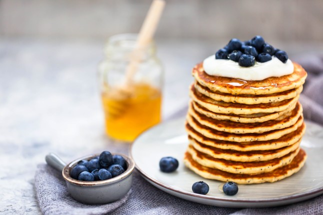 Stack of freshly prepared lemon poppy seed pancakes topped with sour cream and blueberries.
