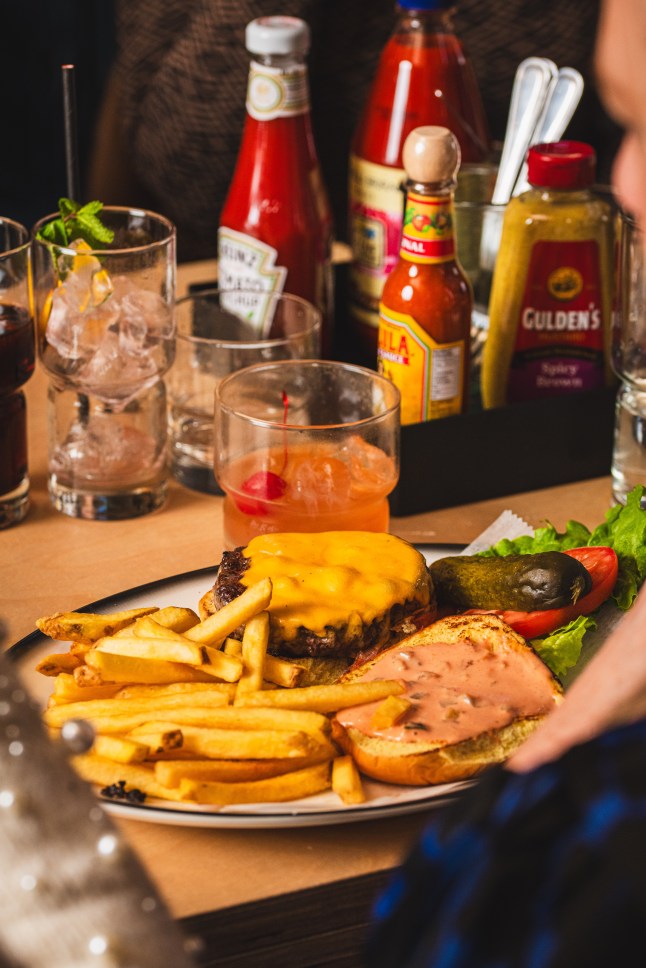 A burger and fries from Black Tap on a table, with condiments in the background