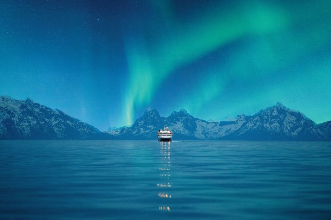 Hurtigruten's MS Nordkapp sailing into the distance with the Northern Lights dancing in the sky.