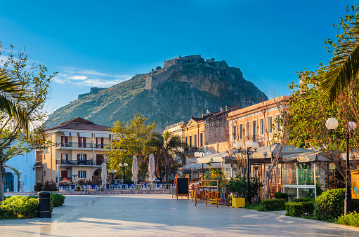 A sunny Philellinon square in Nafplio in the Peloponnese, Greece, with the castle of Palamidi on a hill in the distance.