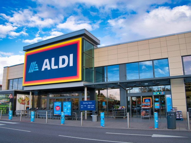The Aldi logo on a shopfront, inside a retail park in the Wirral on a sunny afternoon.