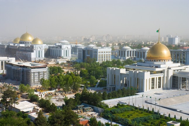A city view in Turkmenistan, showing white buildings with gold domes and green trees.