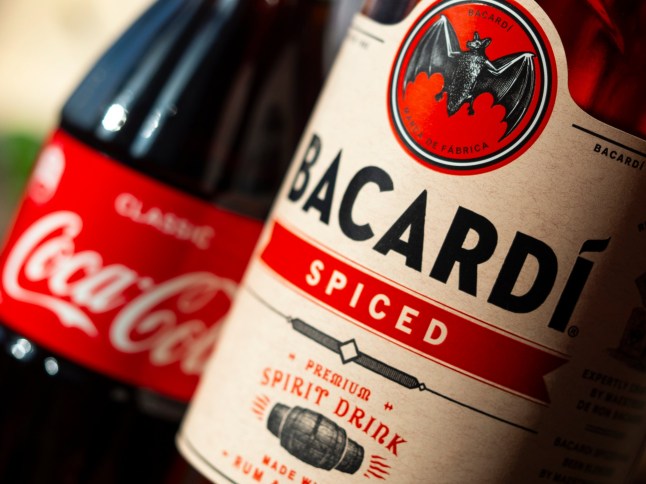KIEV, UKRAINE - January 16, 2021: In this photo illustration seen glass bottle of Coca-Cola and Bacardi spiced rum; Shutterstock ID 1895064382; purchase_order: -; job: -; client: -; other: -