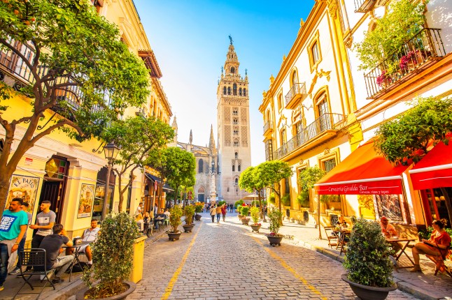 A sunny street in Seville, Spain, with a church at the end and red awnings over the shops