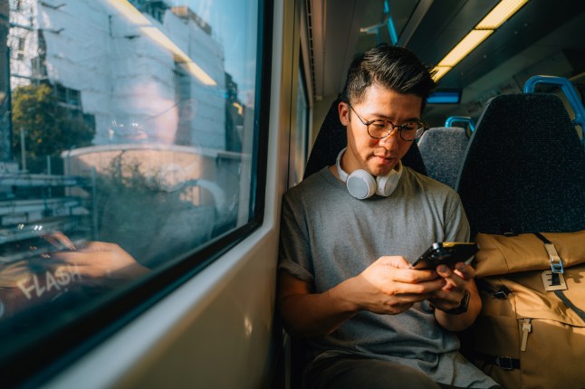Young man sitting on the train while using his smartphone.