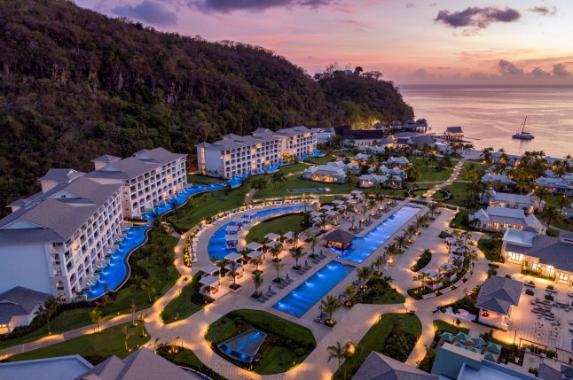 A sunset view over Sandals Saint Vincent and the Grenadines resort, with buildings, pools and lounge areas next to the ocean.