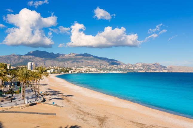 A sandy beach in Altea, Spain, with mountains in the background under a blue sky.