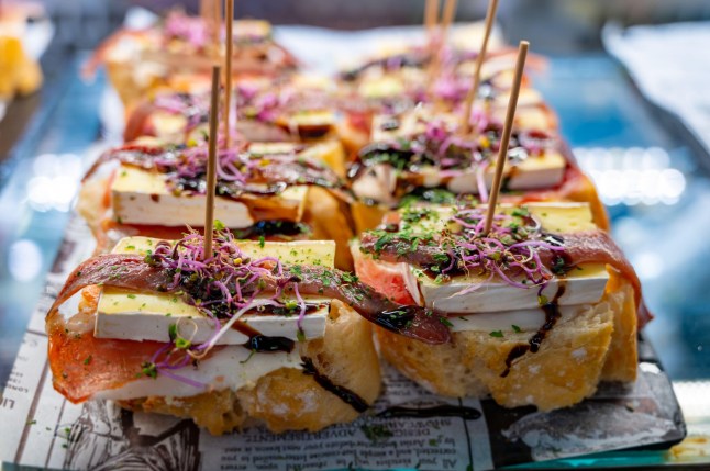 Typical snack of Basque Country, pinchos or pinxtos skewers with small pieces of bread, sea food, eggs, cheese, jamon served in bar in San-Sebastian